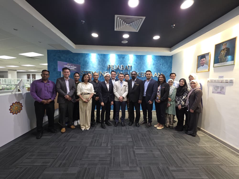 Group photograph of MHNexus and PERKESO teams in the lobby of the Pejabat Sistem Insurans Pekerjaan, with the Labour Market Exchange wall sign behind them.